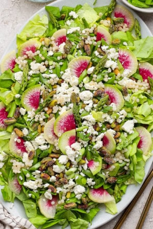 Spring salad with couscous and peas on a large serving platter next to gold silverware.
