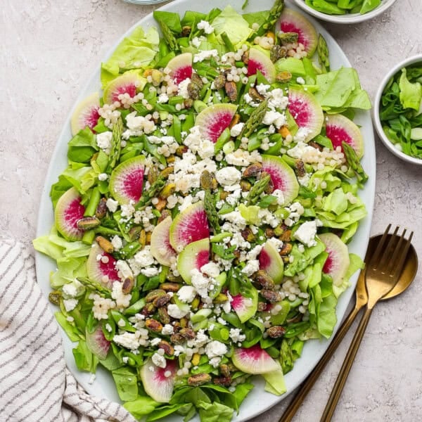 Spring salad with couscous and peas on a large serving platter next to gold silverware.