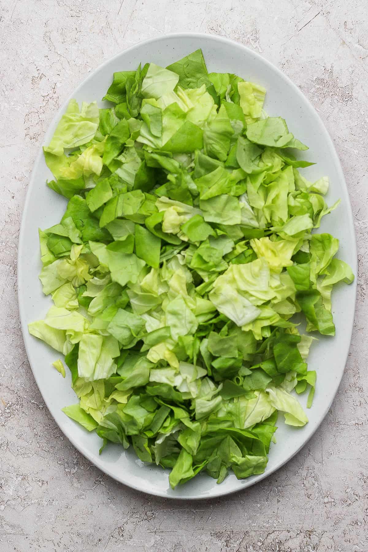 Chopped butter lettuce on a serving platter for a spring salad with couscous and peas.