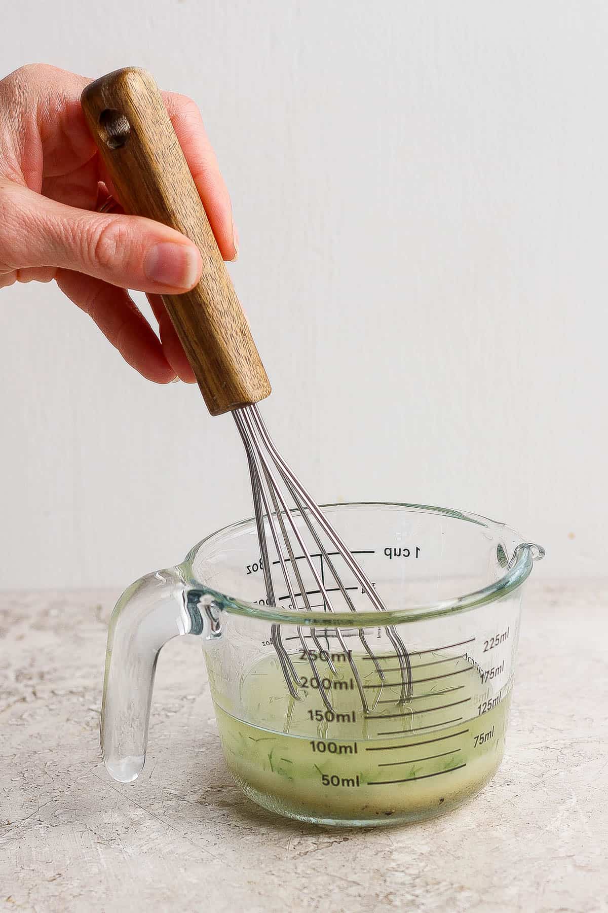 A lemon dill vinaigrette being whisked in a glass measuring cup for a spring salad.