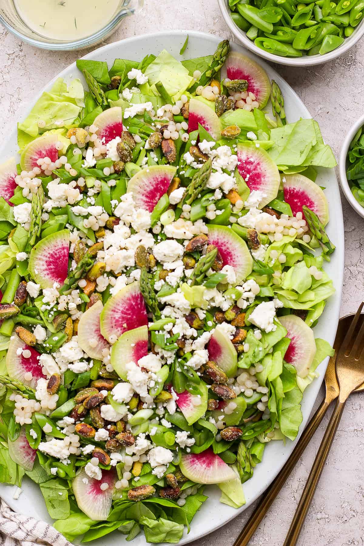 A spring salad with couscous and peas on a large platter next to some gold silverware.