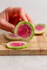 A watermelon radish being cut into slices on a cutting board for a spring salad.