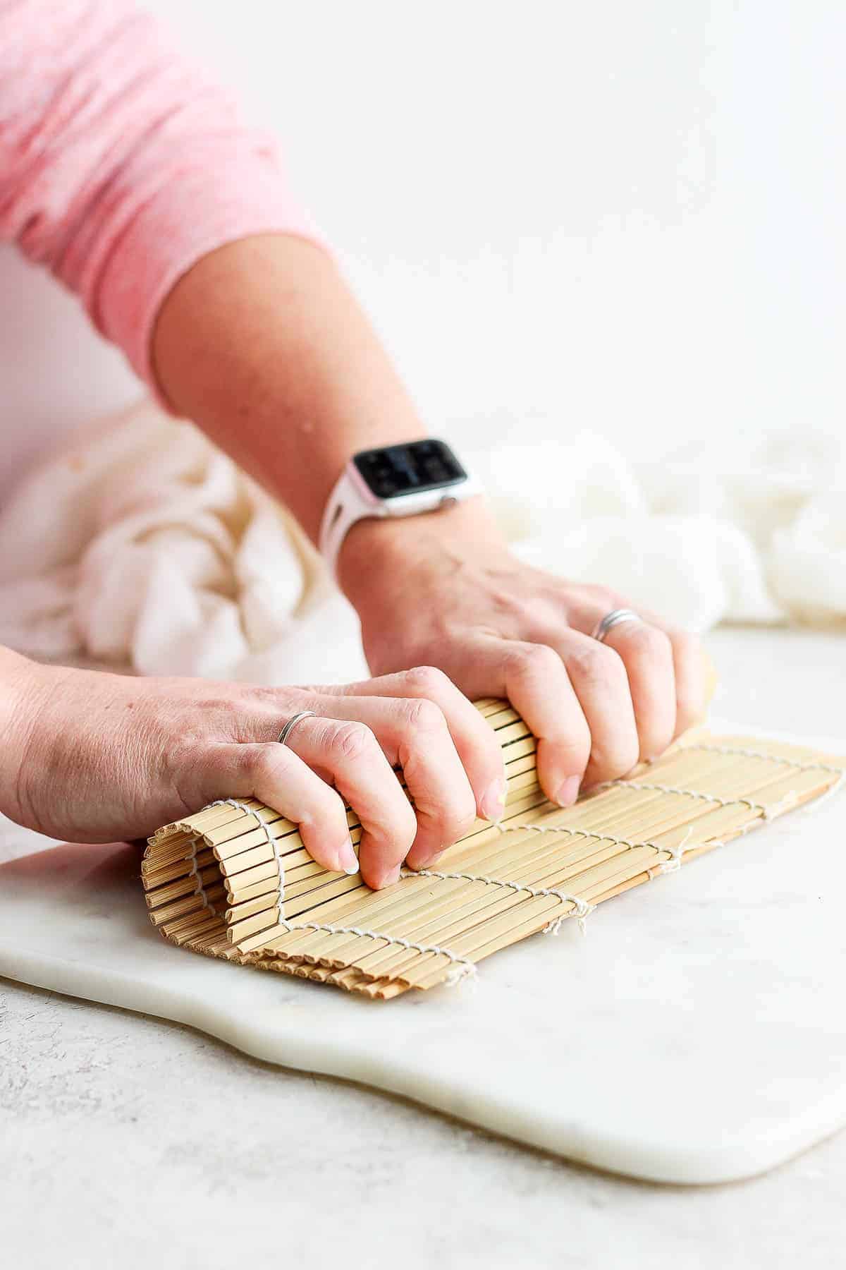 Two hands giving a homemade sushi roll a slight squeeze during the rolling process.