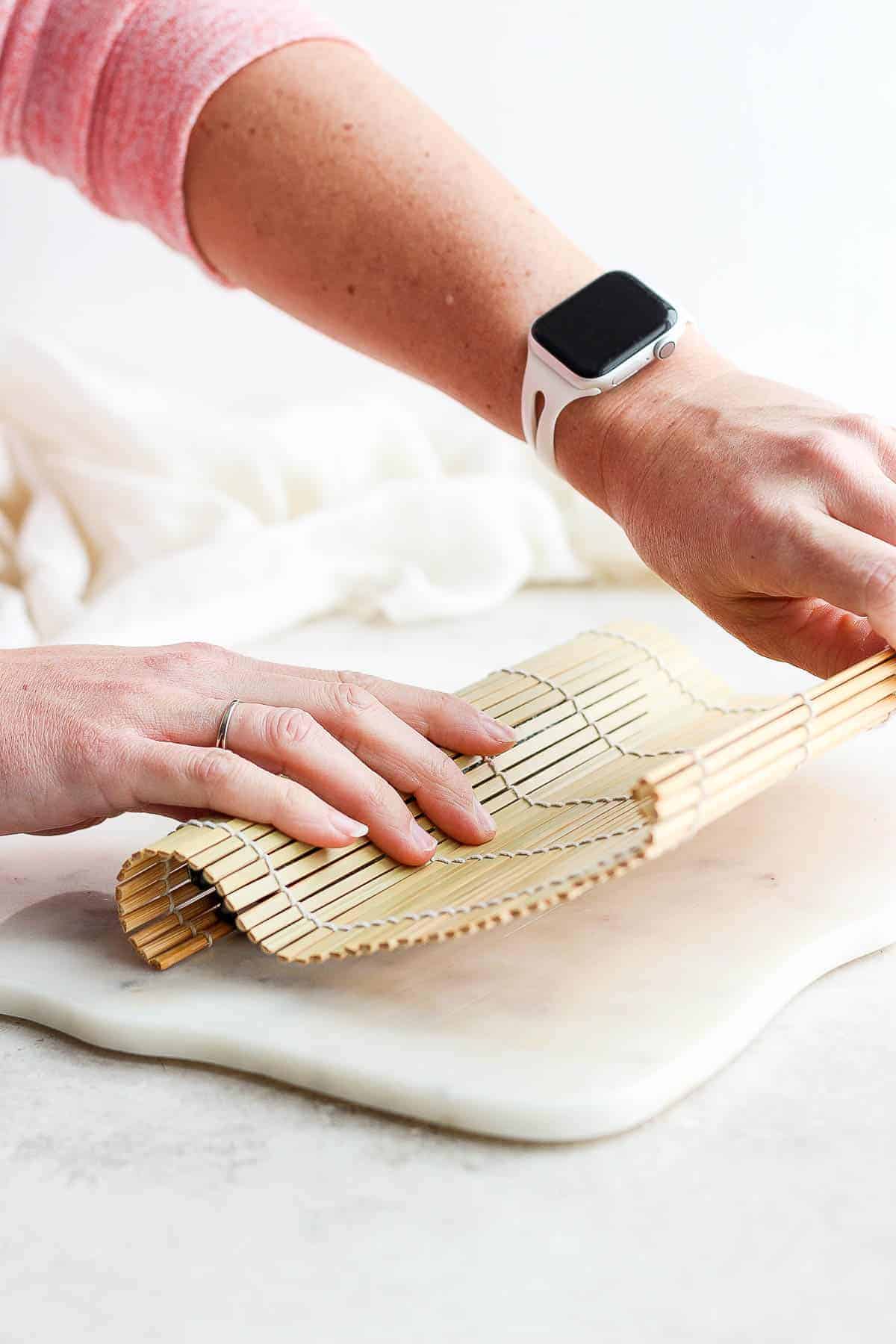 Two hands finishing a homemade sushi roll by rolling out the bamboo mat.