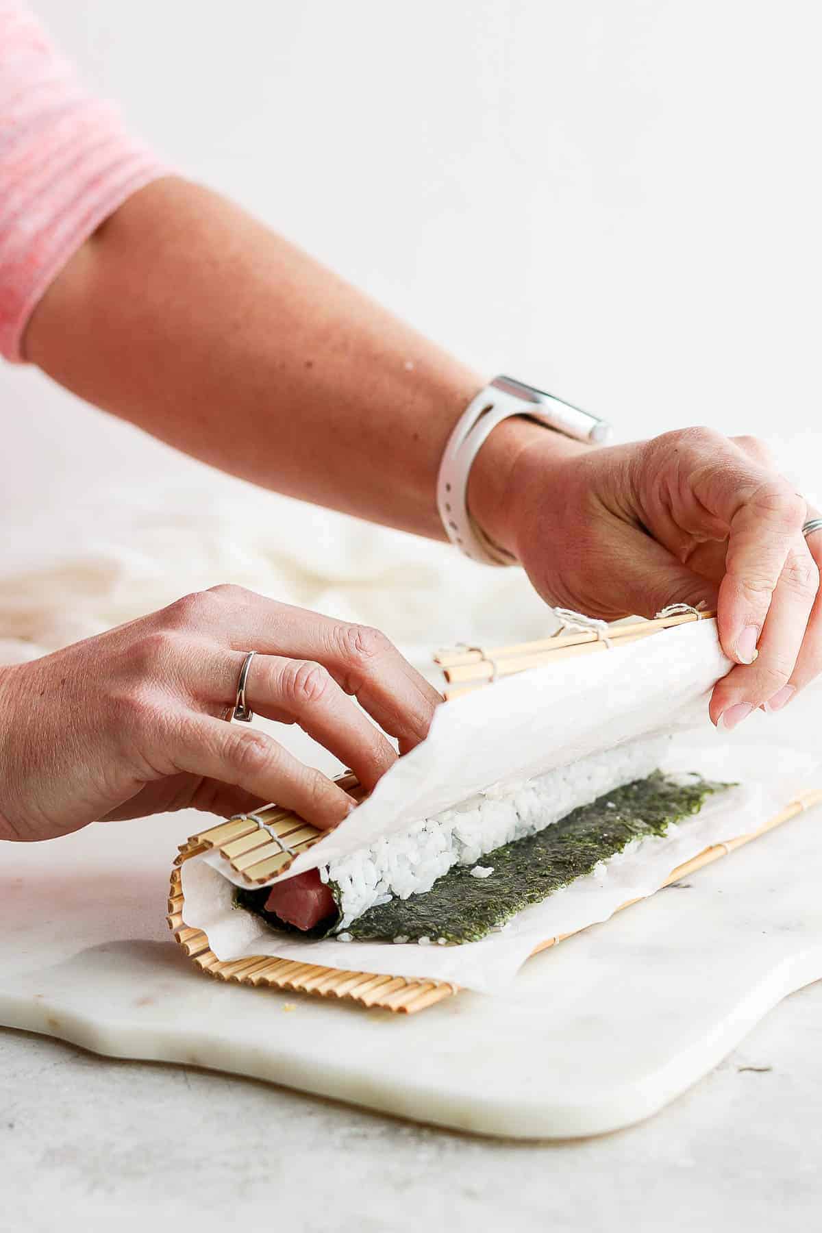 A homemade inside out roll being finished by pulling the parchment paper and bamboo mat away.