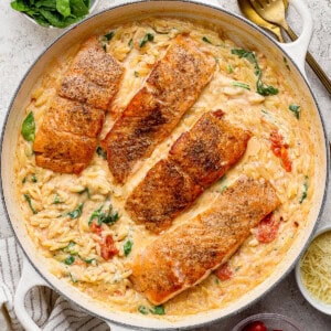 Salmon orzo in a large braising pan next to a gold spoon and some fresh basil.