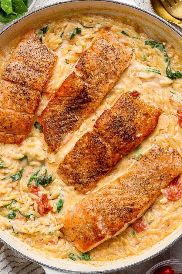 Salmon orzo in a large braising pan next to a gold spoon and some fresh basil.