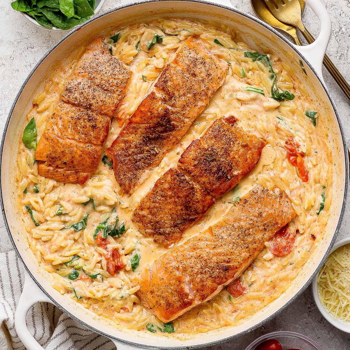 Salmon orzo in a large braising pan next to a gold spoon and some fresh basil.