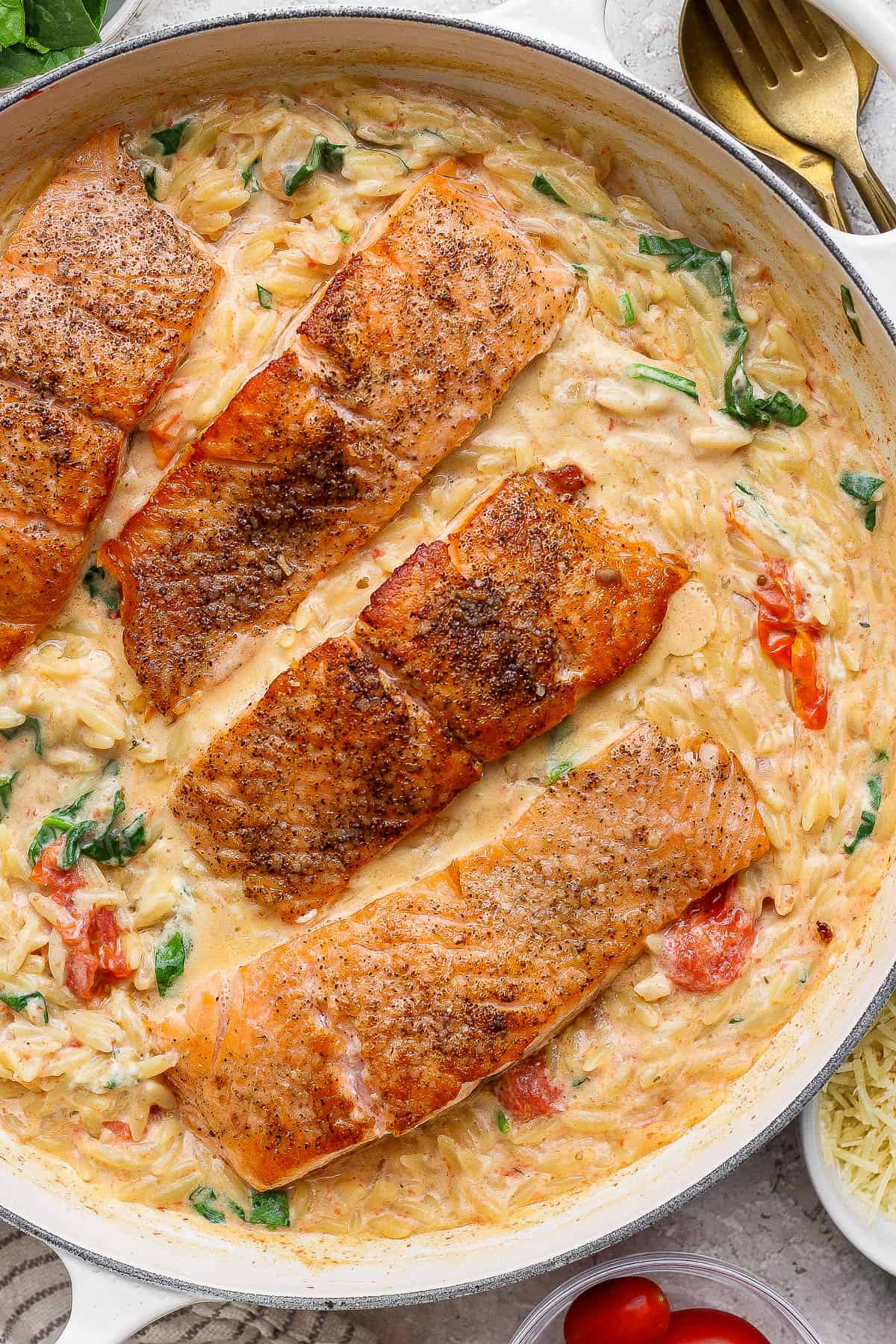A braising pan of fully cooked salmon orzo next to a fork and spoon.