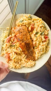 Someone holding a plate of salmon orzo with a gold fork sticking out the side.