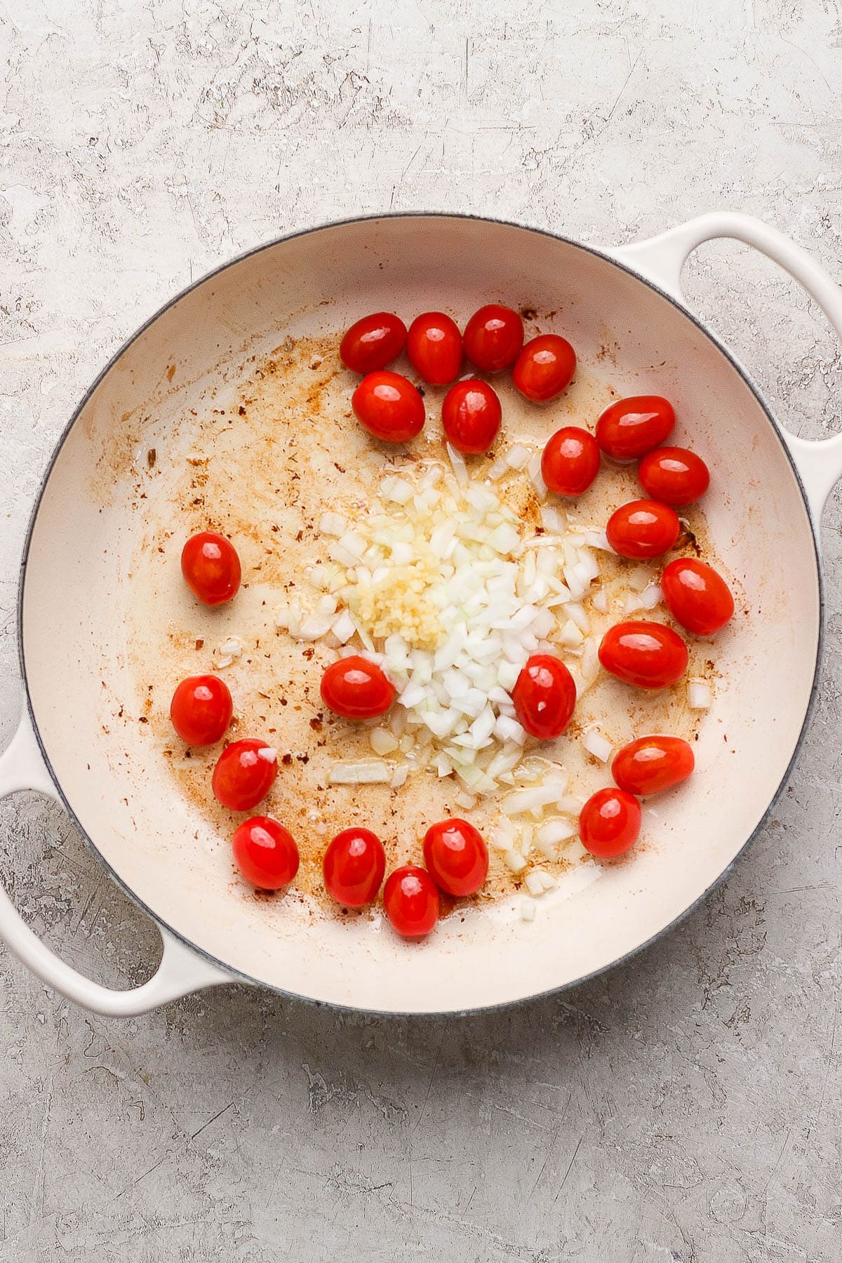 Sautéed tomatoes and onions in a braiser for salmon orzo.