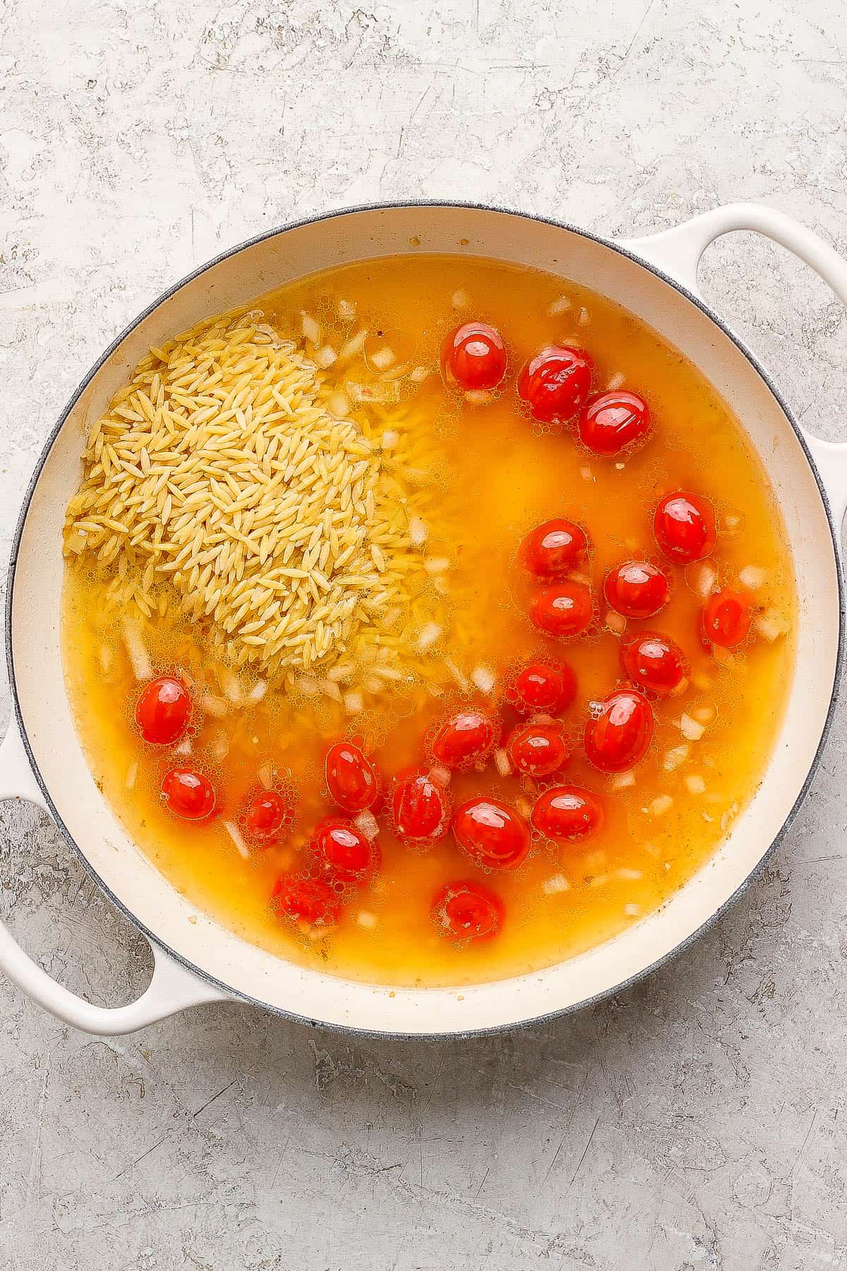 Broth and orzo added to the sautéed tomatoes and onions for salmon orzo.