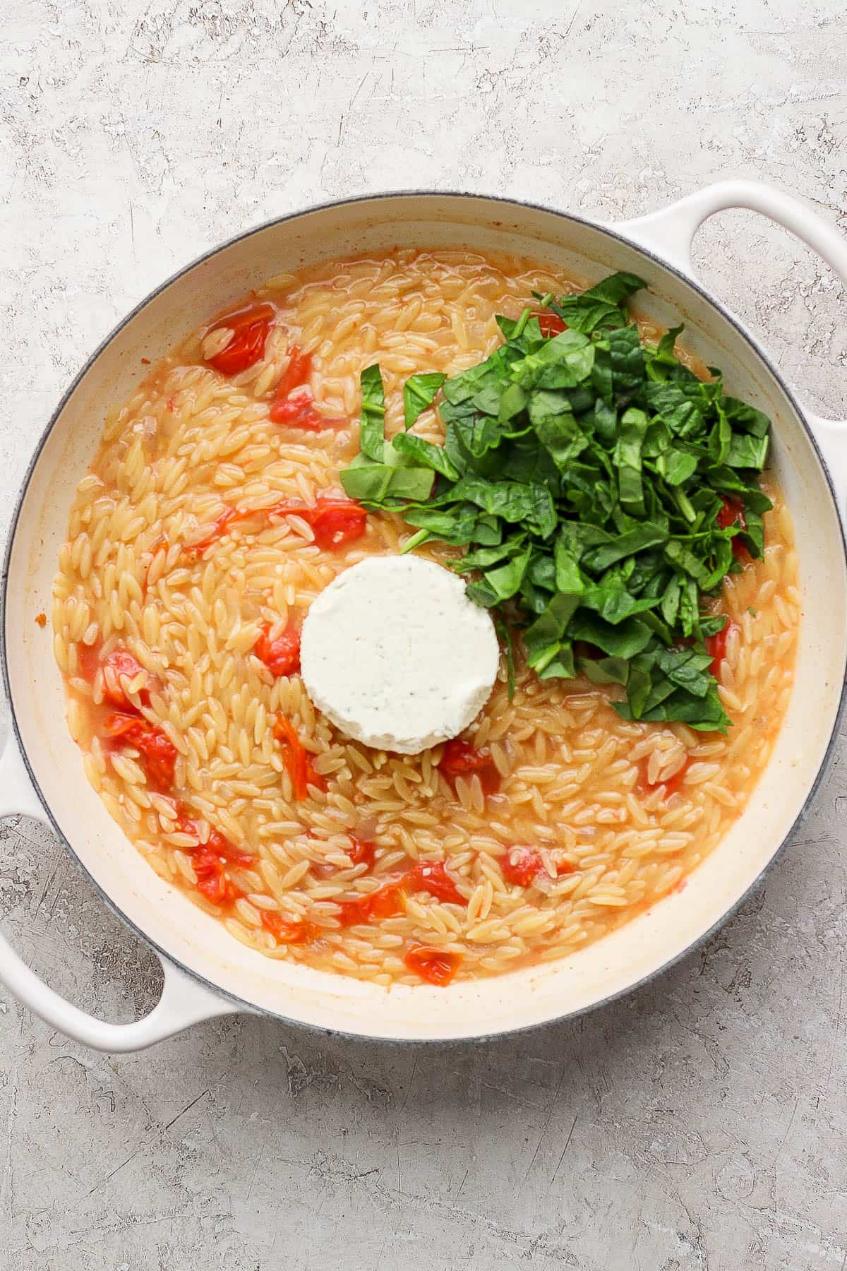 Boursin cheese and spinach added to a braiser of salmon orzo with fully cooked orzo.