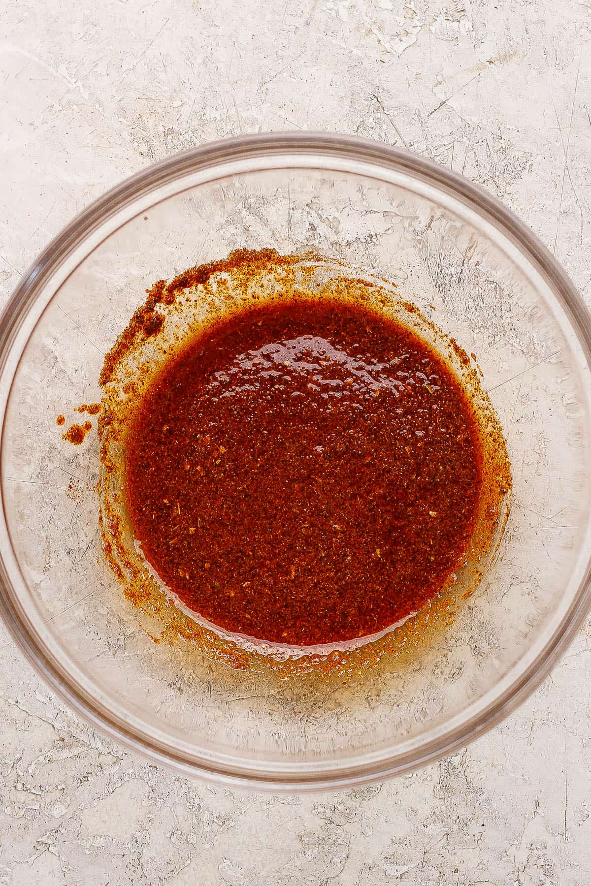 Fajita seasoning mixed in a large glass bowl with olive oil and lime juice for making sheet pan chicken fajita bowls.