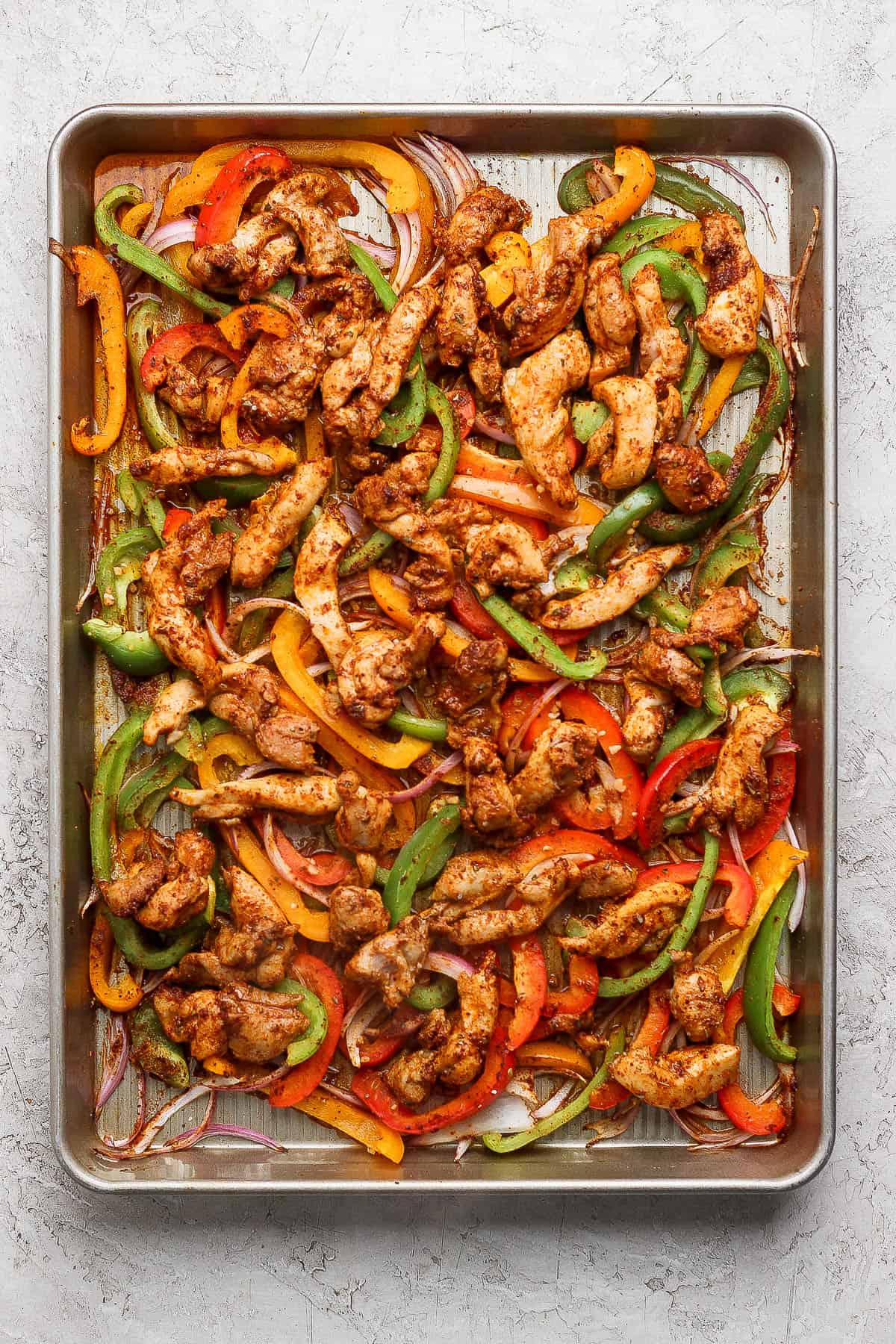 Fully baked chicken and veggies on a sheet pan for sheet pan chicken fajita bowls.