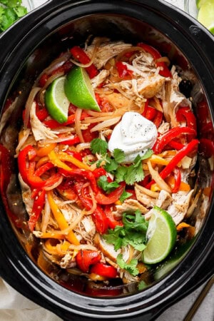 Slow cooker chicken fajitas in the crockpot with some lime wedges and sour cream.