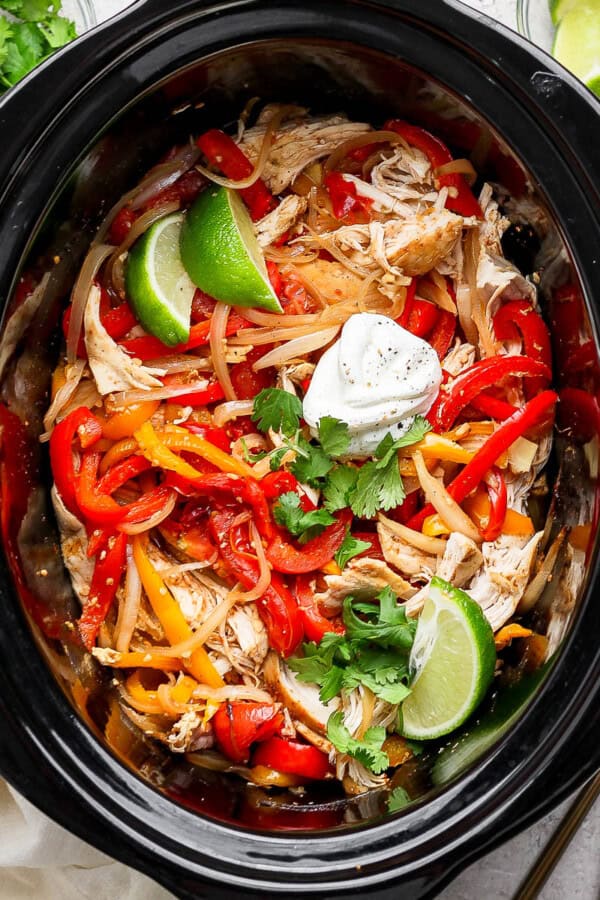 Slow cooker chicken fajitas in the crockpot with some lime wedges and sour cream.