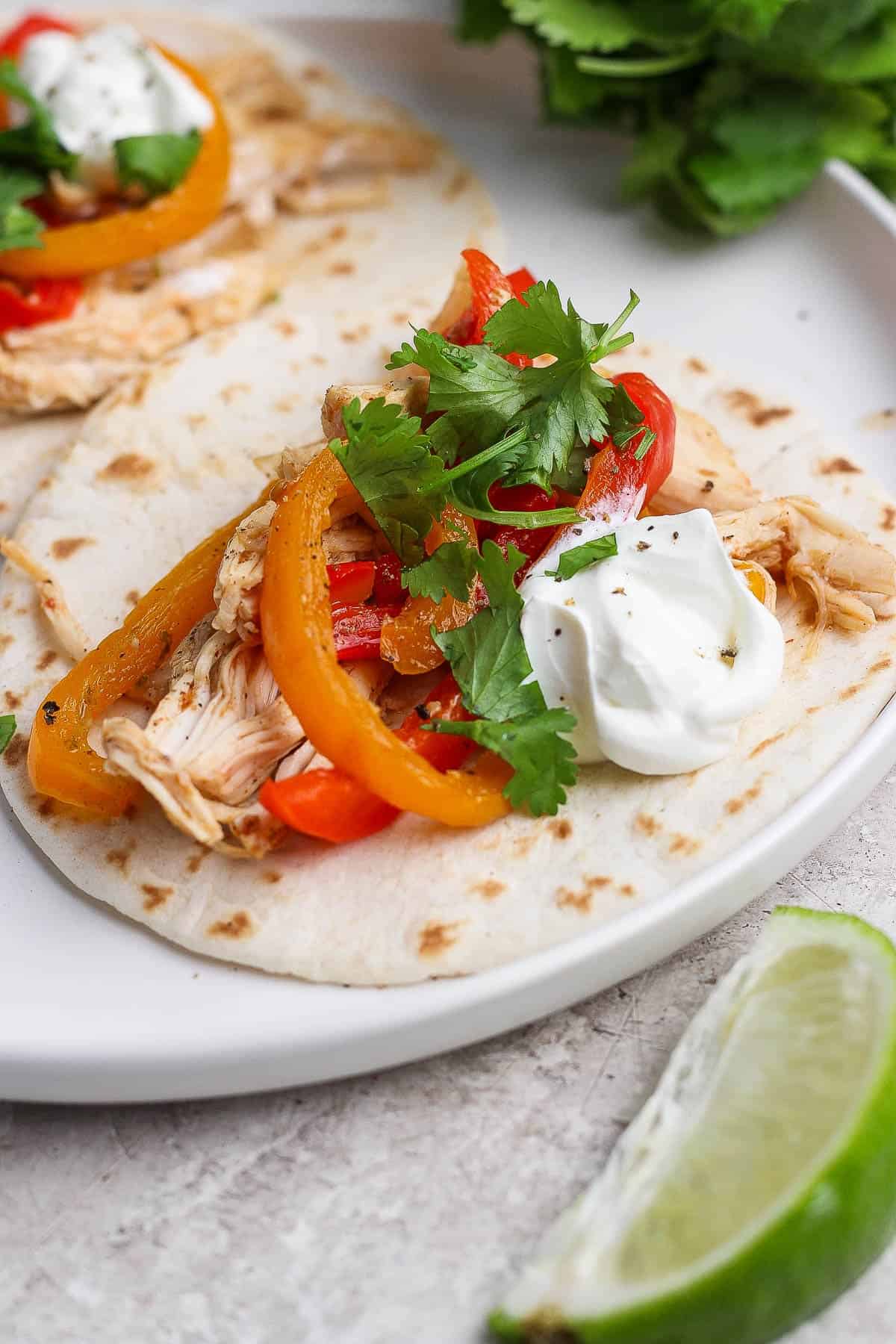 Slow cooker chicken fajitas on a tortilla with sour cream and fresh cilantro.