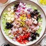 A large bowl of Italian sub in a tub next to a jar of dressing and kitchen towel.