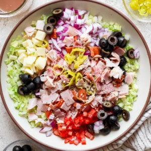 A large bowl of Italian sub in a tub next to a jar of dressing and kitchen towel.