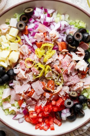 A large bowl of Italian sub in a tub next to a jar of dressing and kitchen towel.