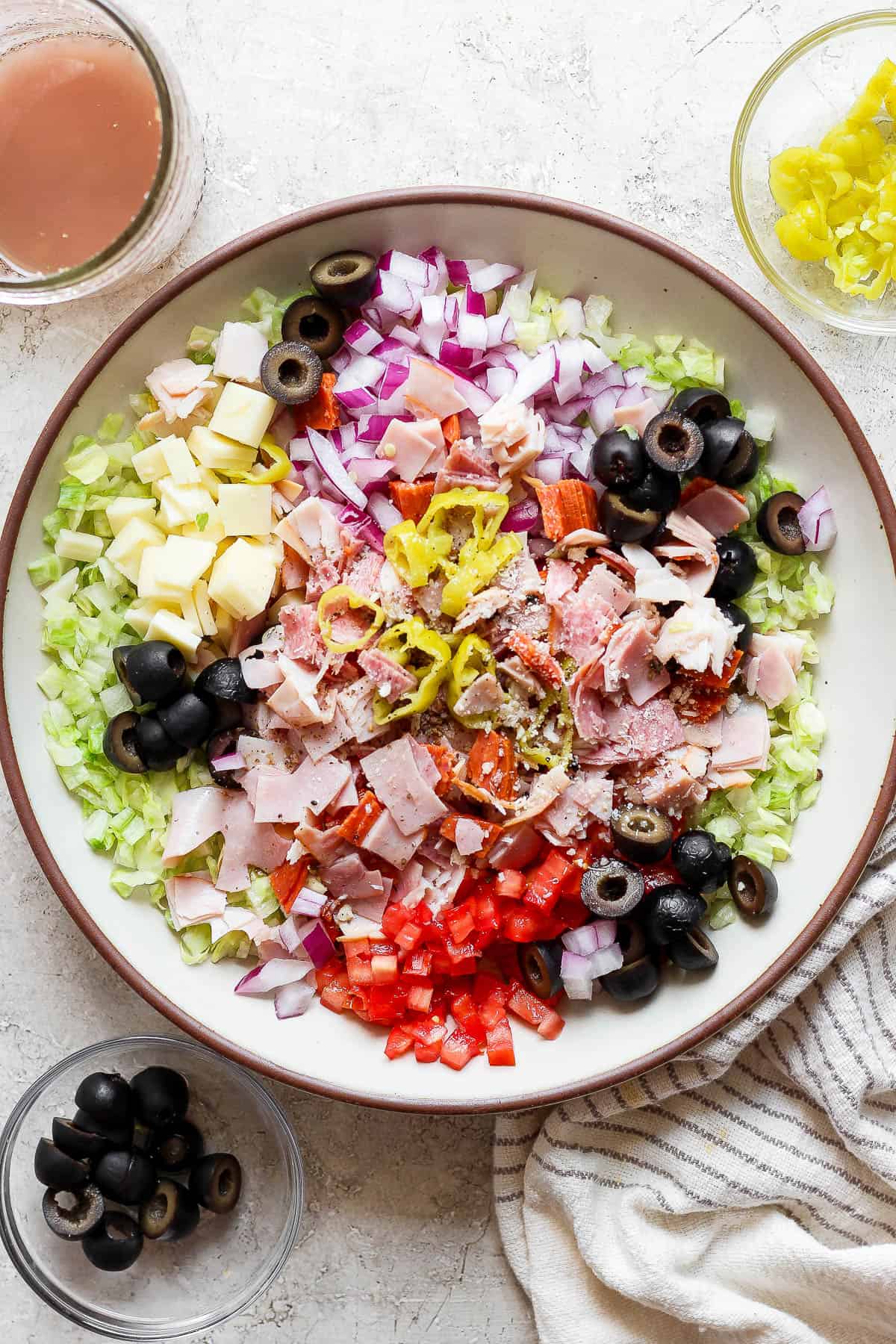 A large serving bowl of a fully assembled Sub in a Tub with small bowls of olives, peperoncini, and dressing.