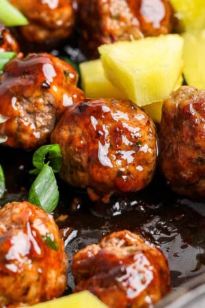 Pineapple teriyaki meatballs in a cast iron skillet with sliced green onions and pineapple chunks.