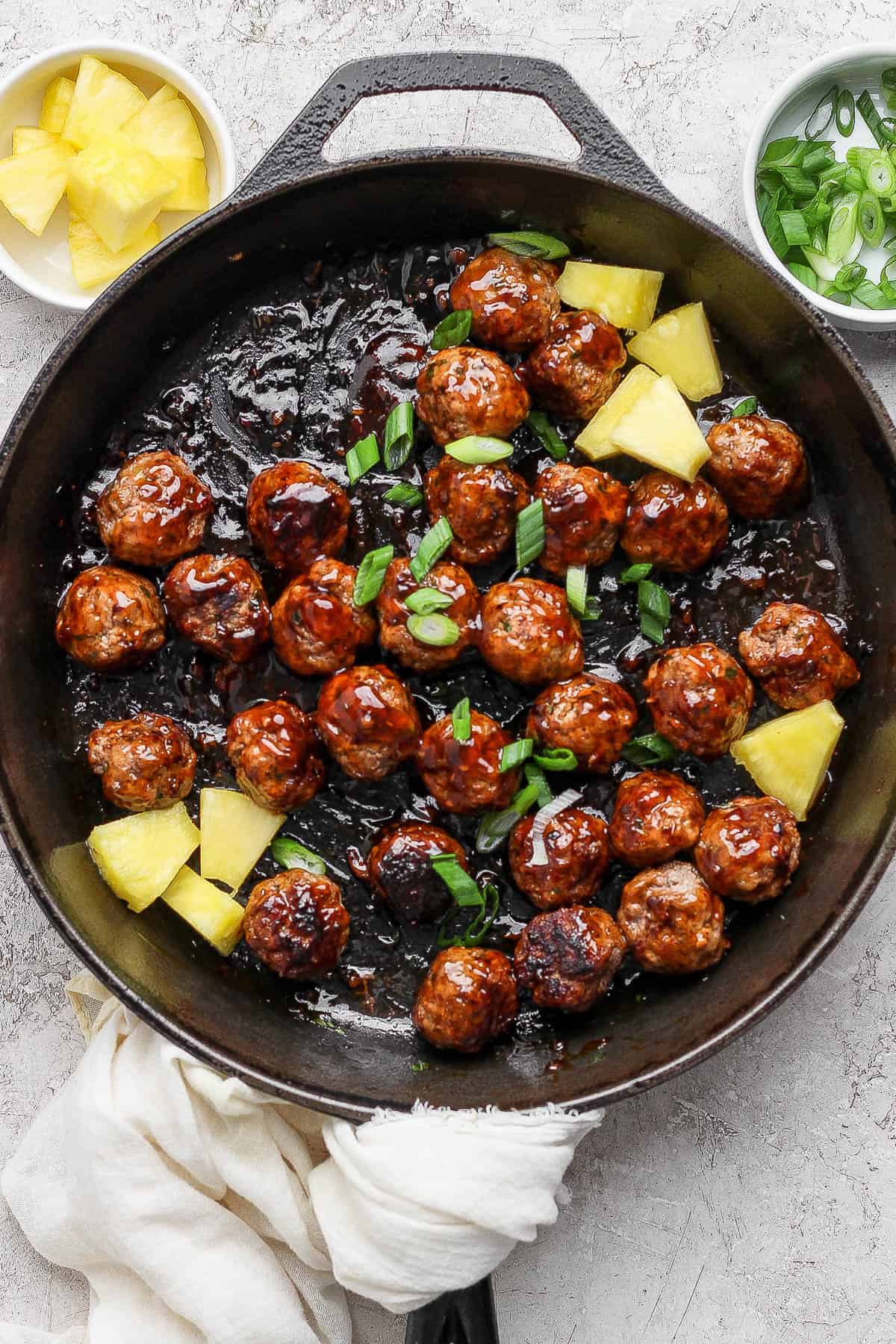 Cooked pineapple teriyaki meatballs in a skillet with teriyaki sauce, pineapple chunks, and sliced green onion.