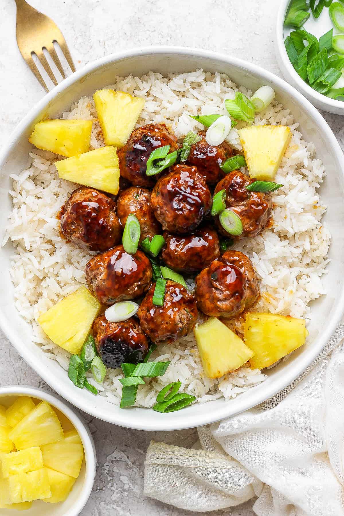 Pineapple teriyaki meatballs served with rice, sliced onions, and fresh pineapple chunks in a bowl.