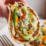 A buffalo chicken smash taco being held over another smash taco on a plate.