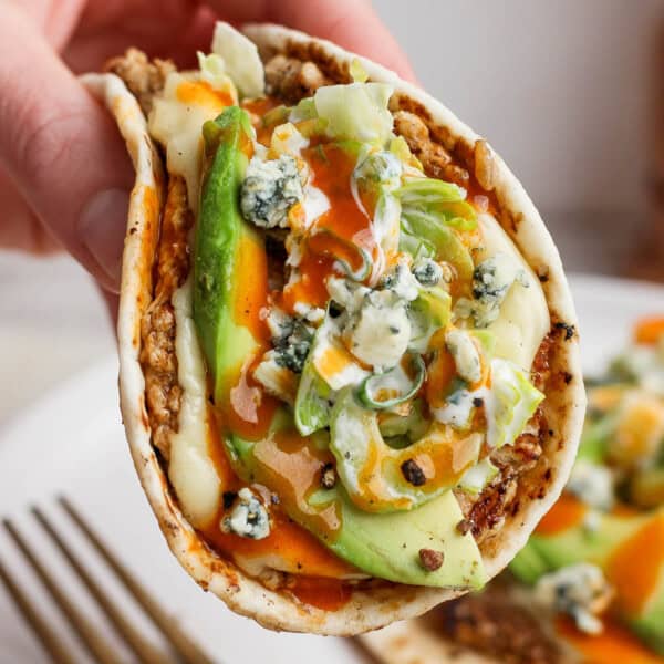 A buffalo chicken smash taco being held over another smash taco on a plate.