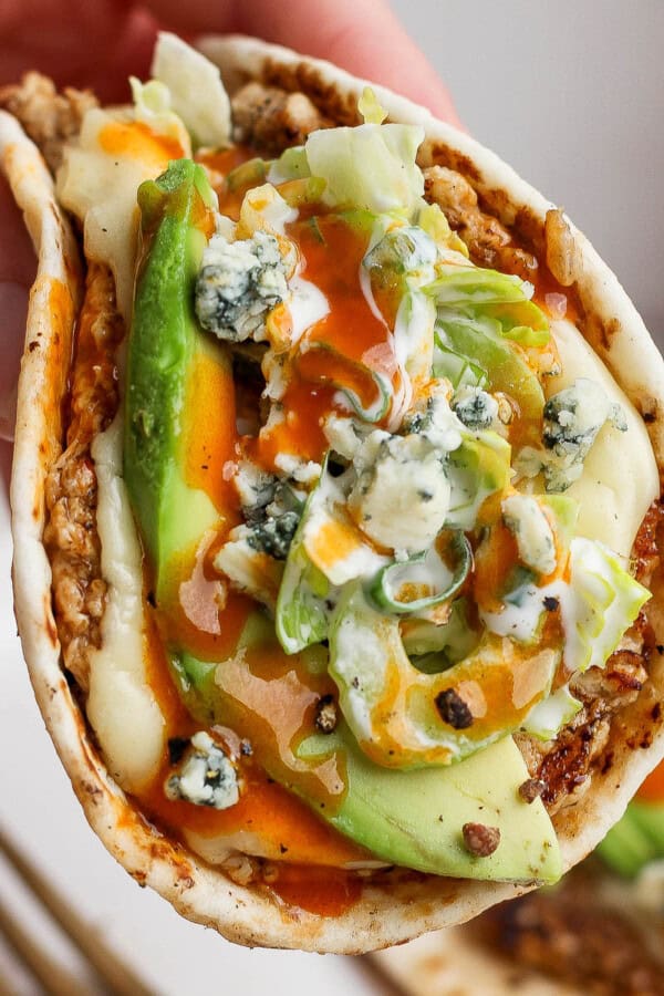 A buffalo chicken smash taco being held over another smash taco on a plate.