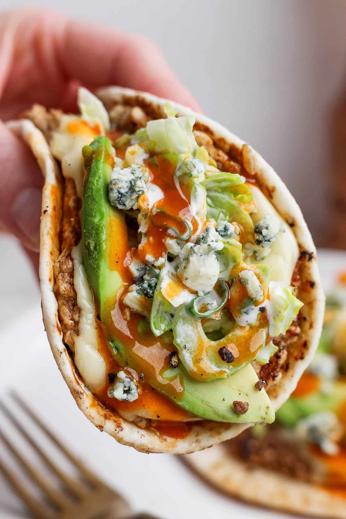 Someone holding a buffalo chicken smash taco over another one on a plate.