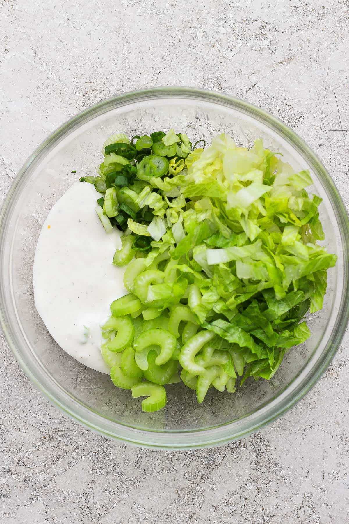 Ingredients for a ranch salad in a glass bowl before being added to buffalo chicken smash tacos.