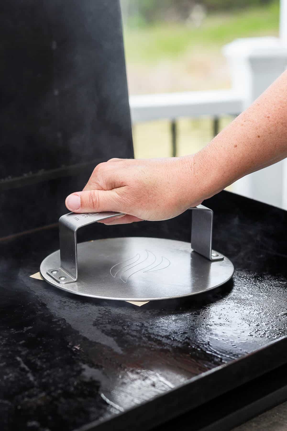 Someone using a burger press to smash a buffalo chicken smash taco burger with parchment paper in between.