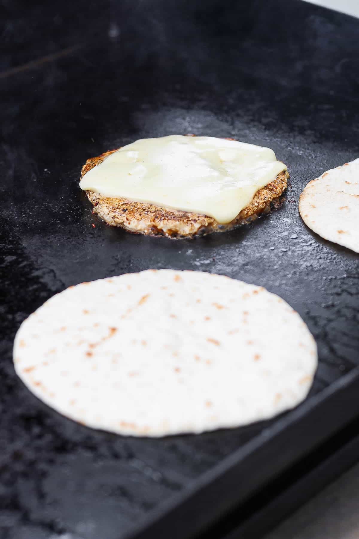 A buffalo chicken smash taco patty with cheese next to a tortilla.