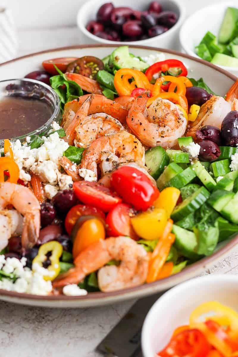 A fully assembled Greek shrimp salad with a small dish of Greek vinaigrette.