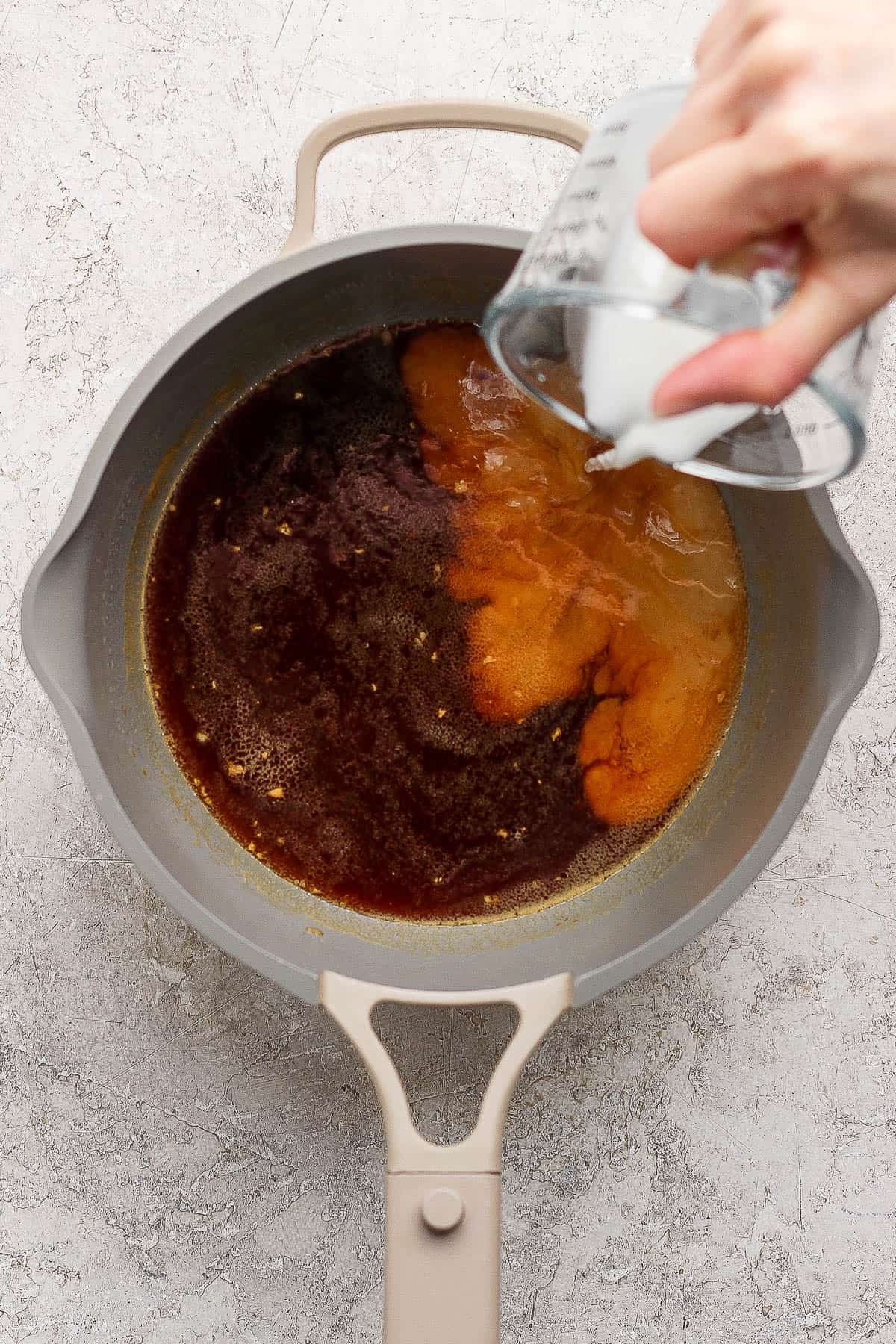 A hand pouring slurry into the pineapple teriyaki sauce mixture in a sauce pan.