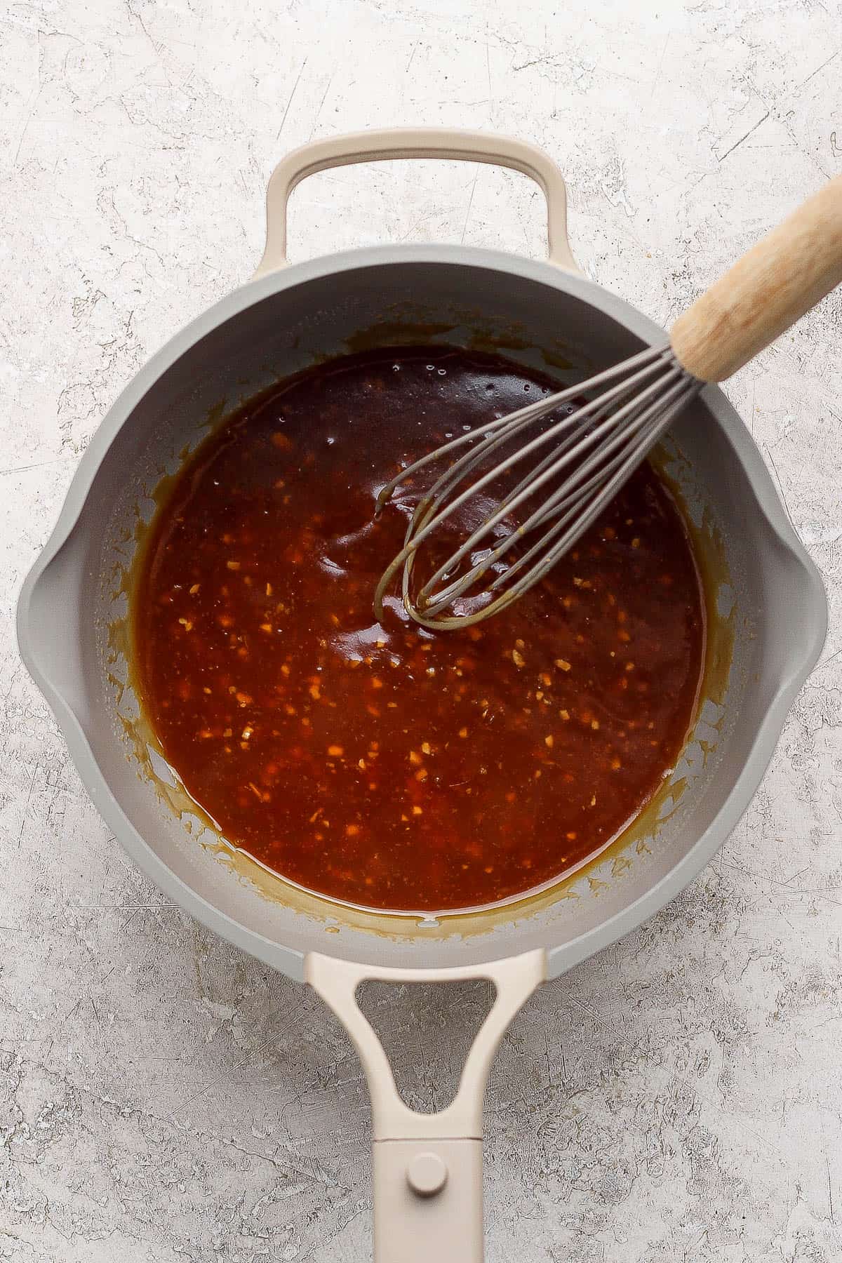 A whisk in a sauce pan of thickened pineapple teriyaki sauce.