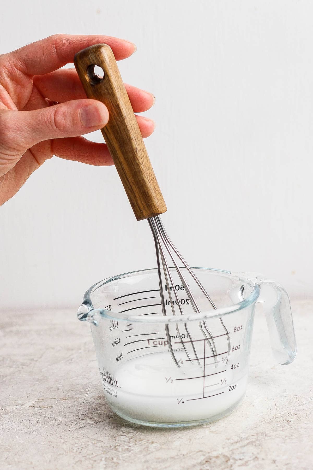 A hand holding a whisk in a measuring cup to make slurry for pineapple teriyaki sauce.