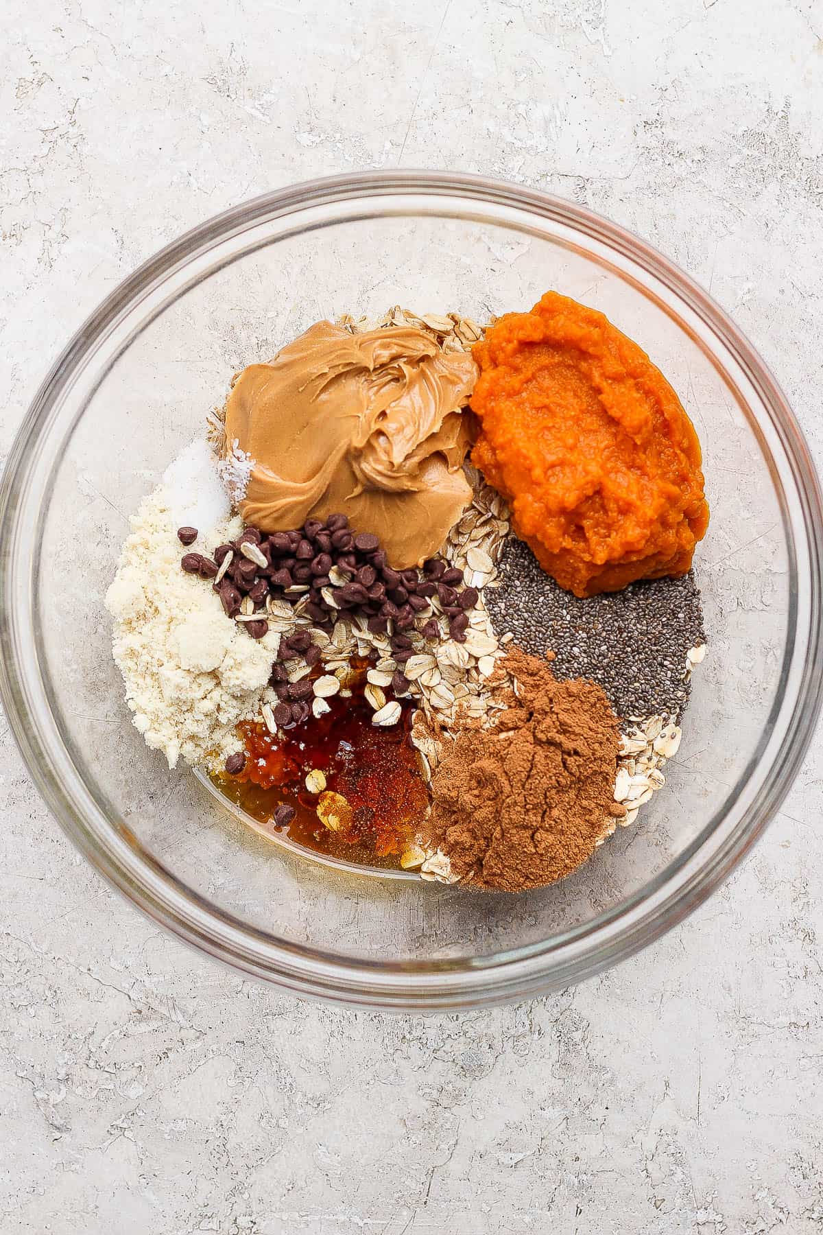 Pumpkin energy ball ingredients of pumpkin puree, peanut butter, almond flour, maple syrup, vanilla extract, pumpkin spice, chia seeds, and oatmeal in a bowl