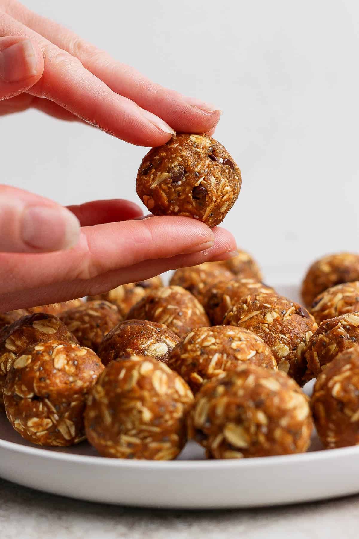 A hand rolling pumpkin energy ball mixture into a ball with a plate of pumpkin energy balls below.