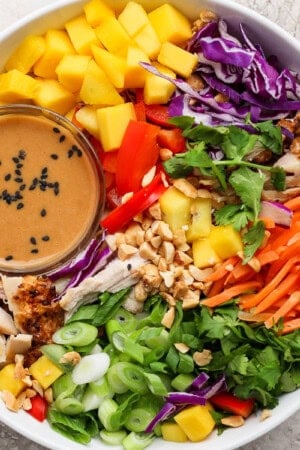 A fully assembled Thai peanut rotisserie chicken salad with a small dish of the dressing.