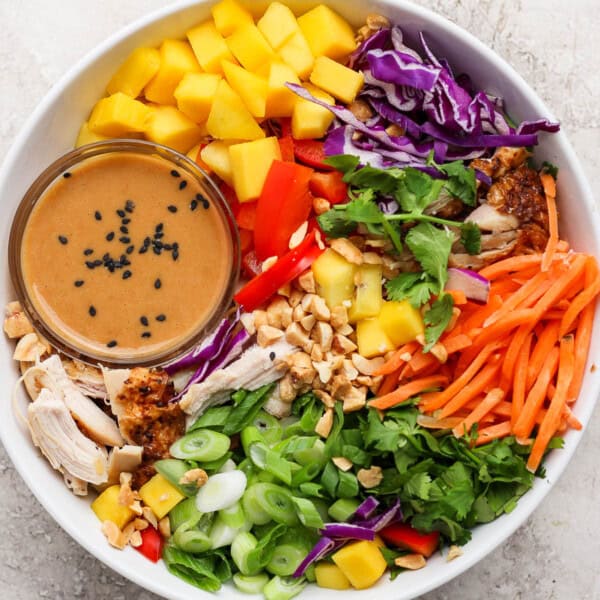 A fully assembled Thai peanut rotisserie chicken salad with a small dish of the dressing.