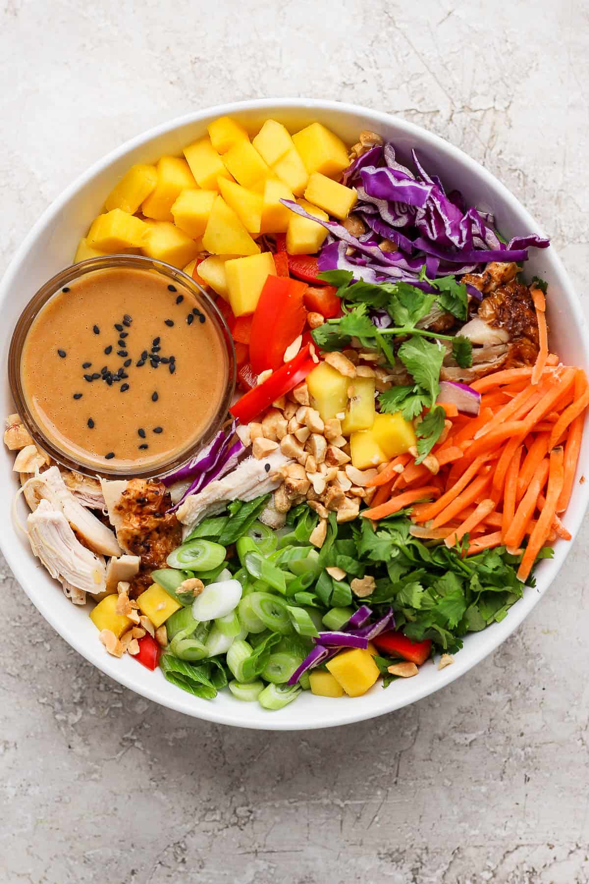 A Thai peanut rotisserie chicken salad in a white bowl with a small dish of peanut dressing.