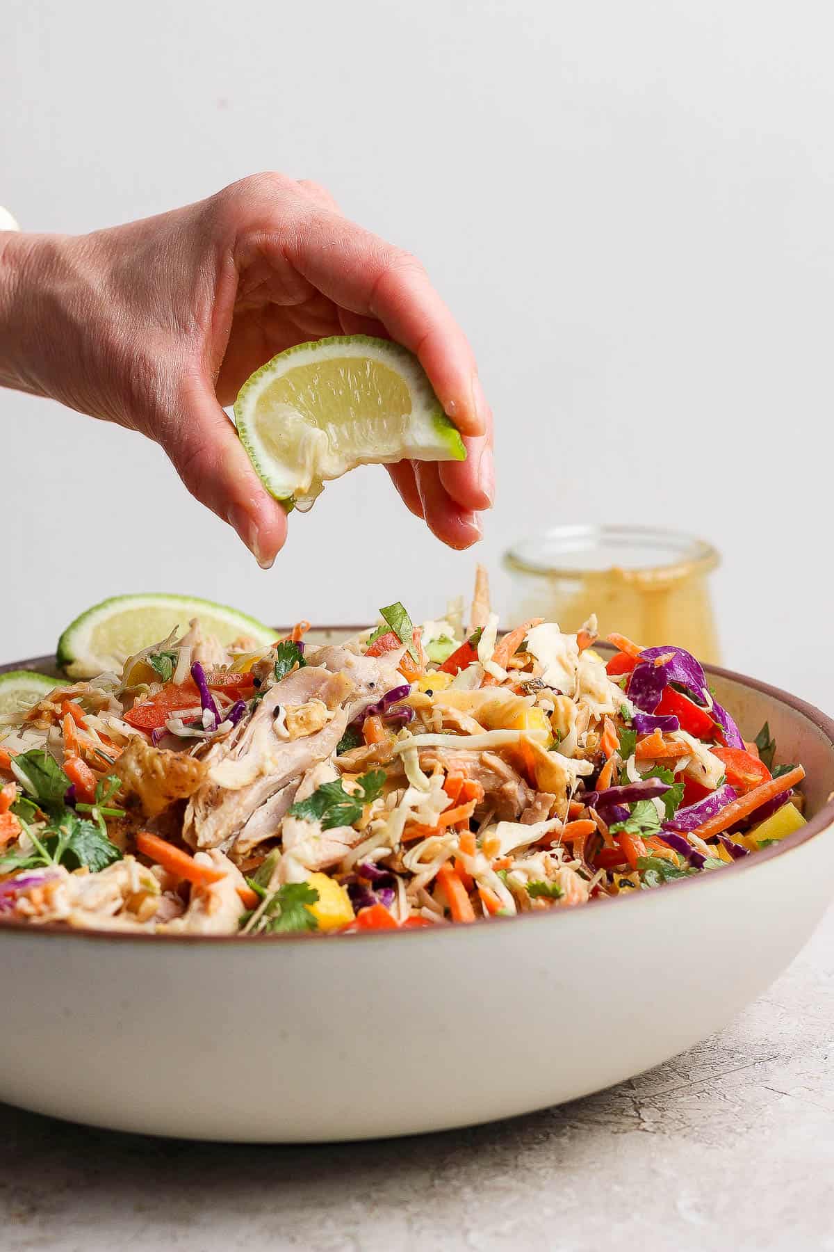A lime wedge being squeezed over a bowl of rotisserie chicken salad.