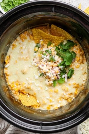 Street corn dip in a slow cooker with a couple tortilla chips sticking out the top.