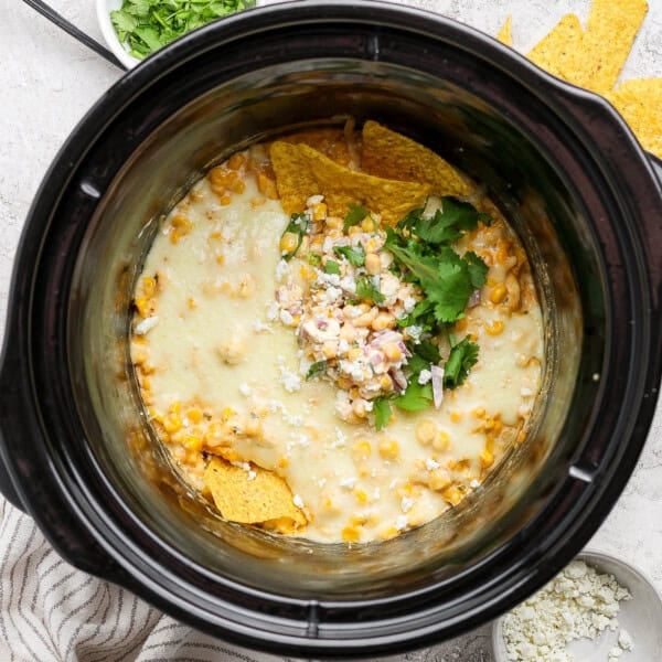 Street corn dip in a slow cooker with a couple tortilla chips sticking out the top.