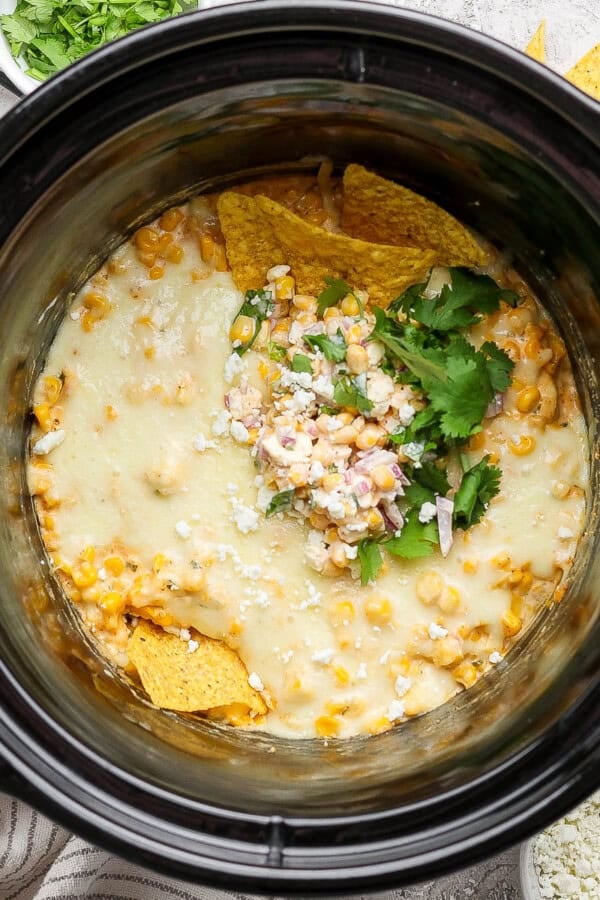 Street corn dip in a slow cooker with a couple tortilla chips sticking out the top.