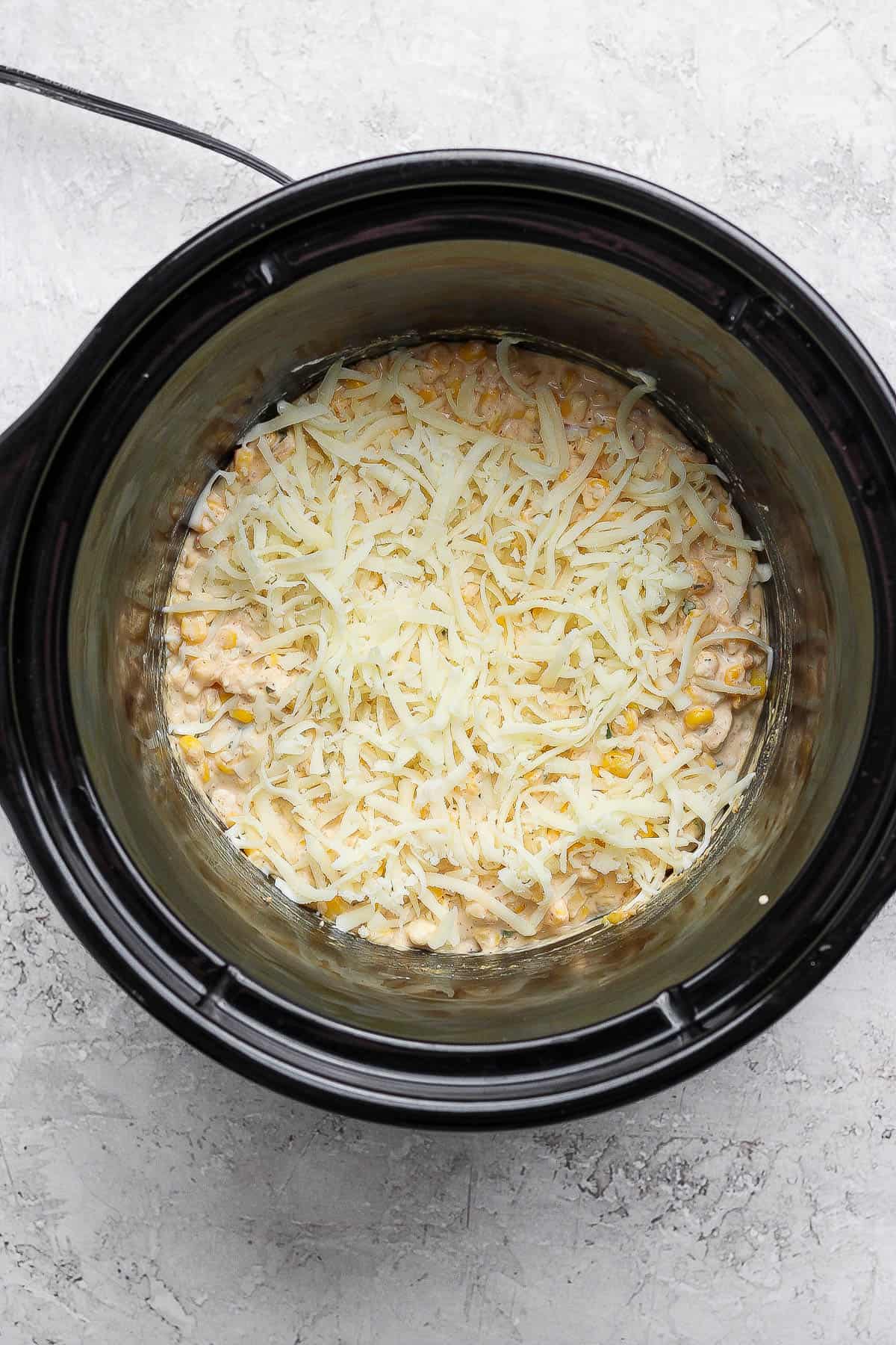 Street corn dip in a crock pot with mozzarella cheese sprinkled on top.